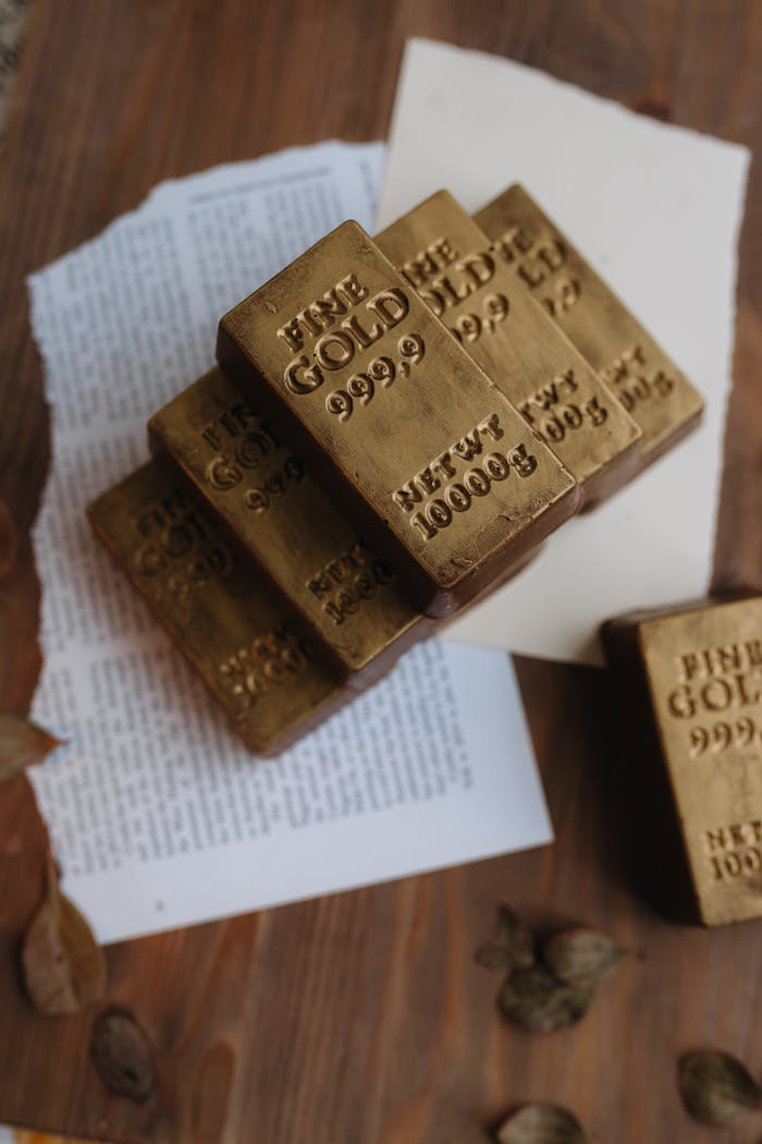 A stack of gold bars imprinted with 'FINE GOLD 999.9' on a wooden surface with papers and nuts.